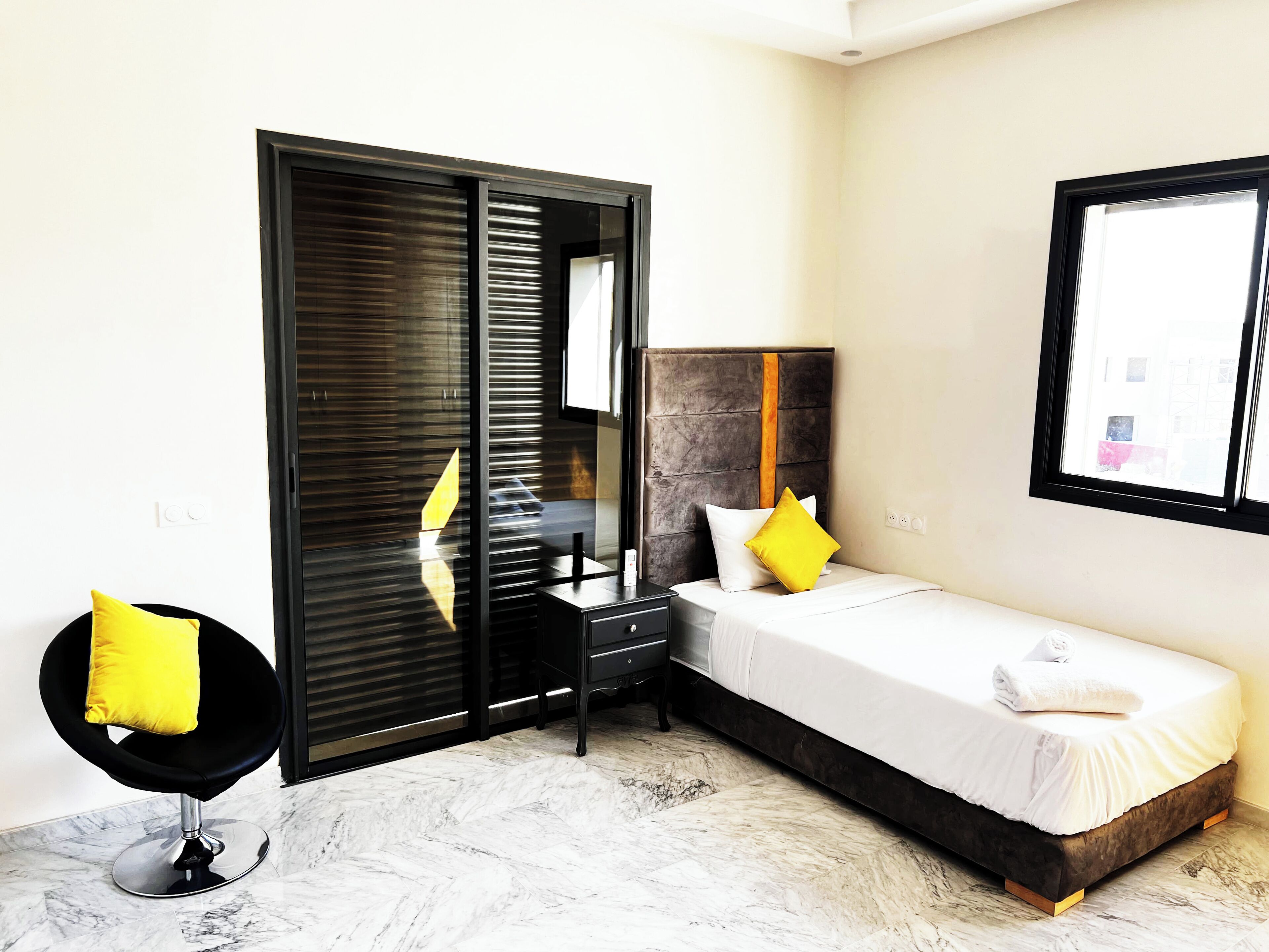 A modern bedroom with a bed, bedside table, and a chair with yellow cushions.