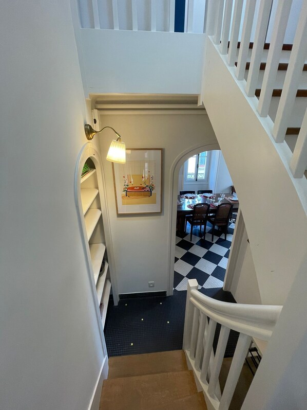 A staircase with white railings leading to a dining area with a checkered floor. - Vacation rental at the foot of the Château de Clisson (Clisson)