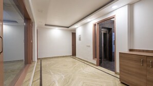 A hallway with a marble floor, a wooden cabinet, and an elevator. - The Gleam Hotel (Gurugram)