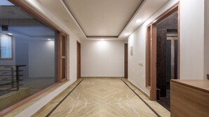A hallway with a marble floor, wooden doors, and a glass partition on the left. - The Gleam Hotel (Gurugram)