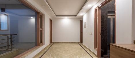A hallway with a marble floor, wooden doors, and a glass partition on the left.