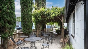 An outdoor patio with round tables and chairs, surrounded by tall trees and a wooden fence. - Historic charm with modern amenities (Colonial Beach)