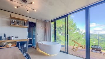 A modern bathroom with a freestanding bathtub, a built-in shower, and a large window offering a view of the outdoors.