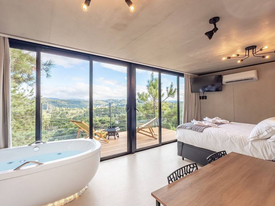A modern bedroom with a large window, a bathtub, a bed, and a dining area.