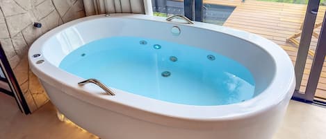 A freestanding hot tub with a clear blue interior, positioned on a wooden deck with a glass balustrade.