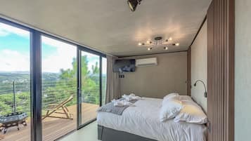 Une chambre moderne avec un grand lit, un luminaire au plafond et une vue sur un balcon agrémenté d’une table et de chaises.