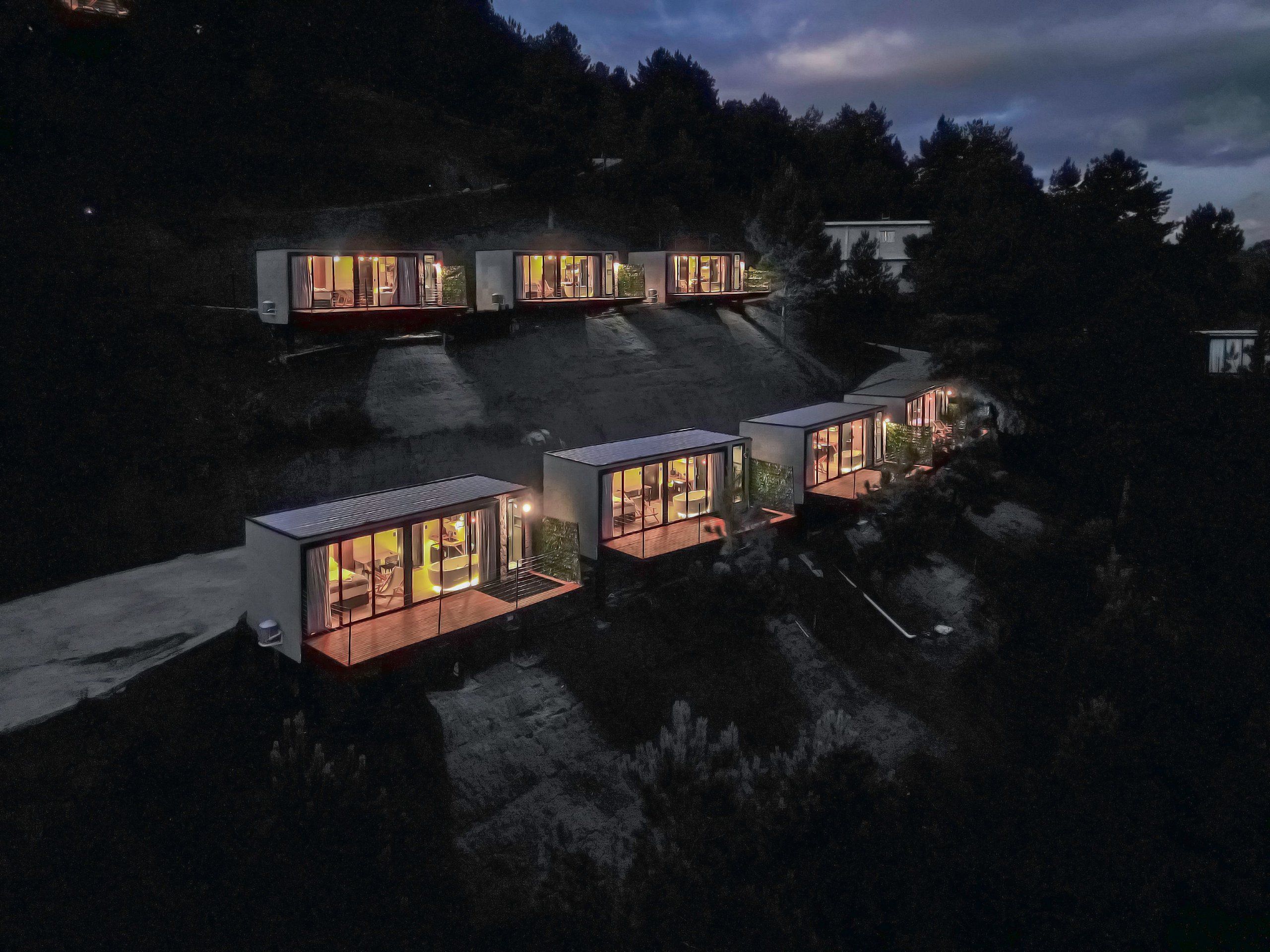 Une série de cabanes modernes à façade vitrée, dotées d’espaces de détente en plein air, disposées sur une colline.