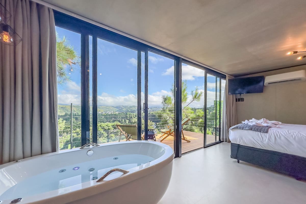 Quarto moderno com uma banheira grande, uma cama e varanda com vista.