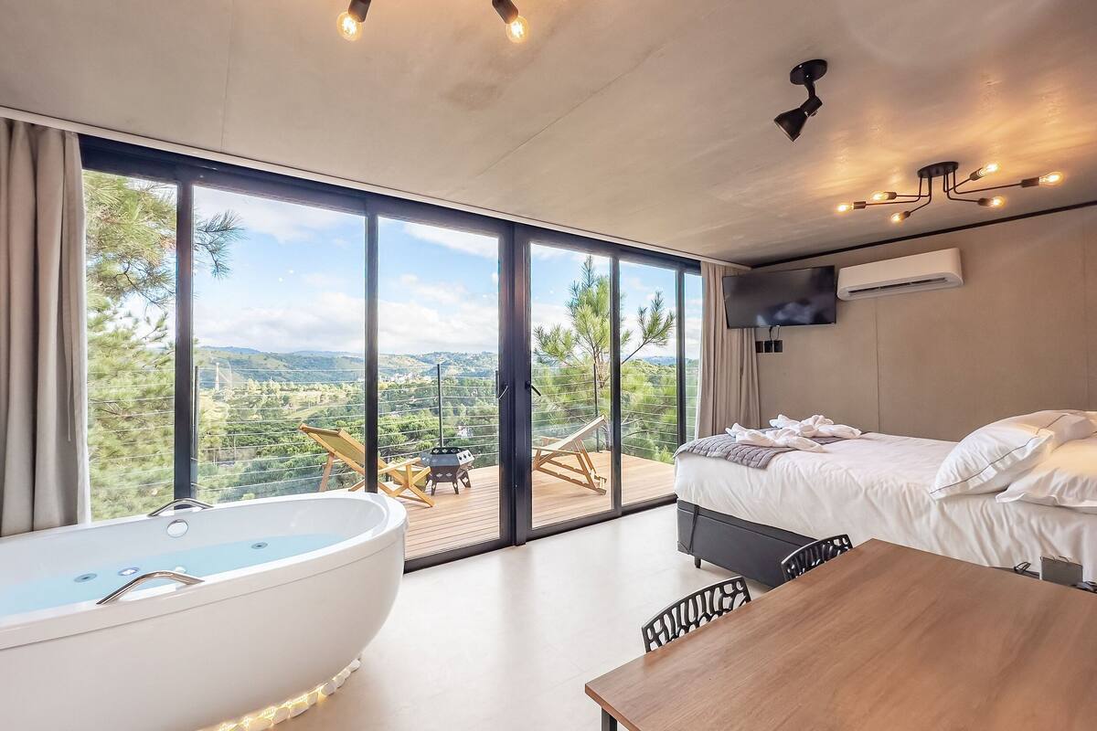Quarto moderno com uma janela grande, uma banheira, uma cama e um espaço de refeições.