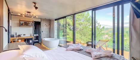 A modern bedroom with a large bed, a bathtub, and a view of the outdoors.