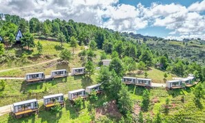 A series of modern, glass-roofed cabins arranged in a semi-circular pattern on a hillside, surrounded by lush greenery and trees. - CNB Cabanas Vista Serra Campos do Jordão (Campos do Jordão)