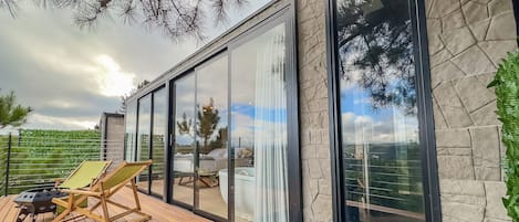 Una terraza moderna al aire libre con piso de madera, una parrilla y dos sillones de descanso.