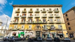 A multi-story building with balconies, a ground-level shop, and parked cars. - Casa Raffaela with Terrace by Wonderful Italy (Naples)
