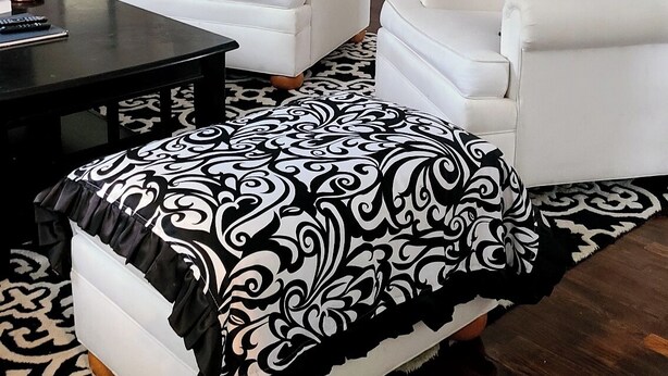 Una sala de estar moderna con dos sofás blancos, una mesa de centro negra y un reposapiés estampado.