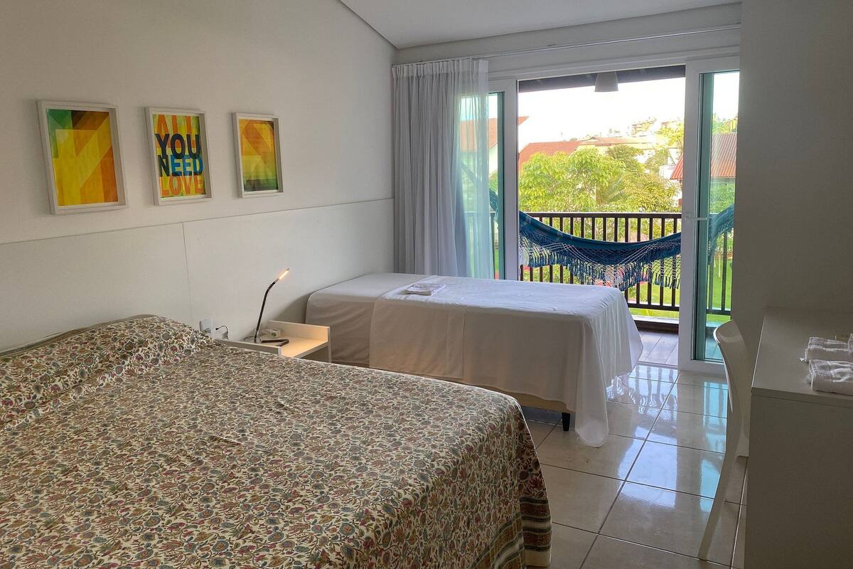 Ein Hotelzimmer mit einem großen Bett, einem kleineren Bett, einem Schreibtisch und einem Balkon mit einer Hängematte.