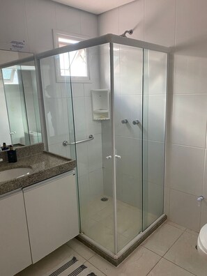 Een moderne badkamer met een douchecabine van glas, een wastafel met granieten blad en een klein raam.
