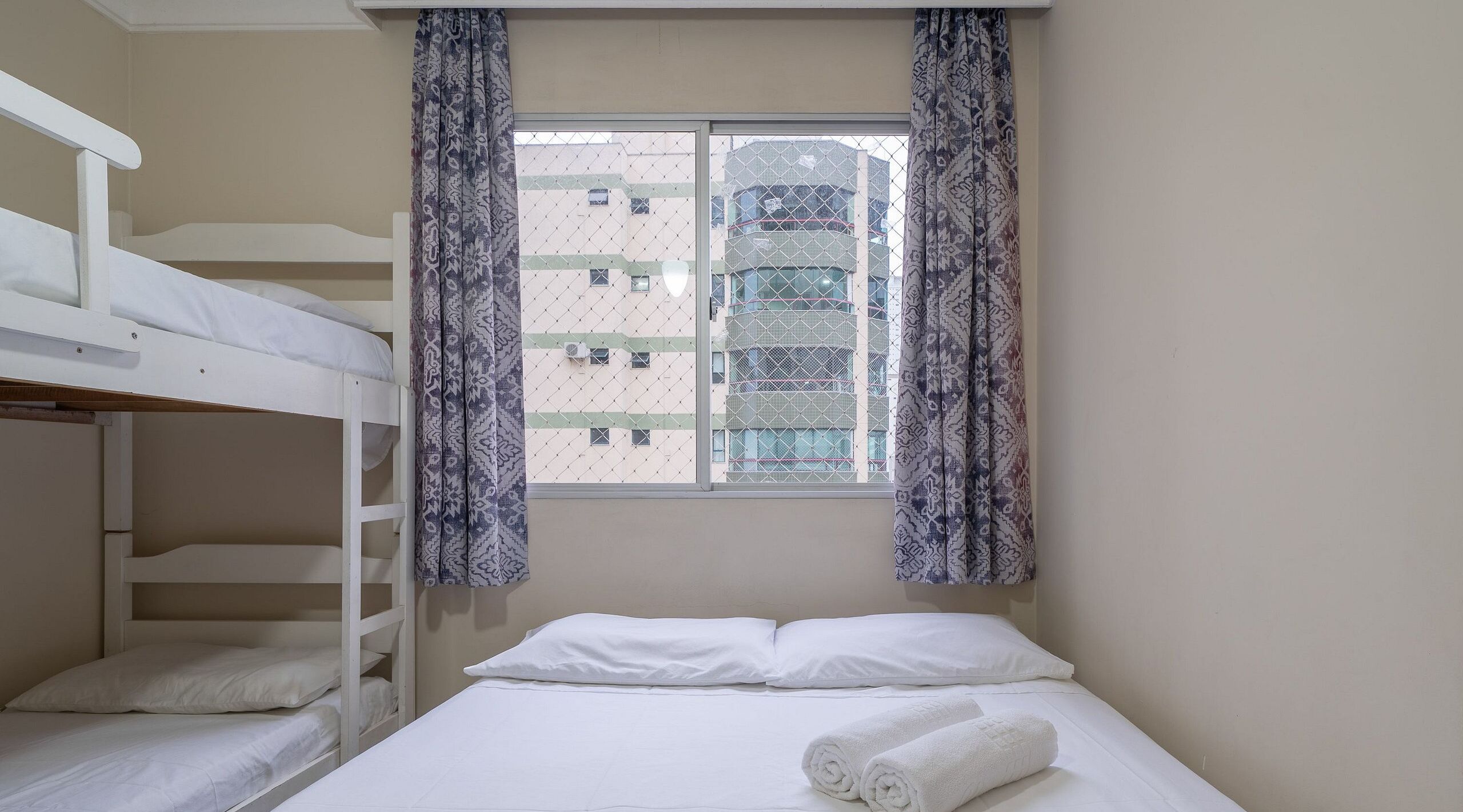 Une chambre avec des lits superposés, une fenêtre avec des rideaux à motifs et un lit avec des serviettes enroulées.