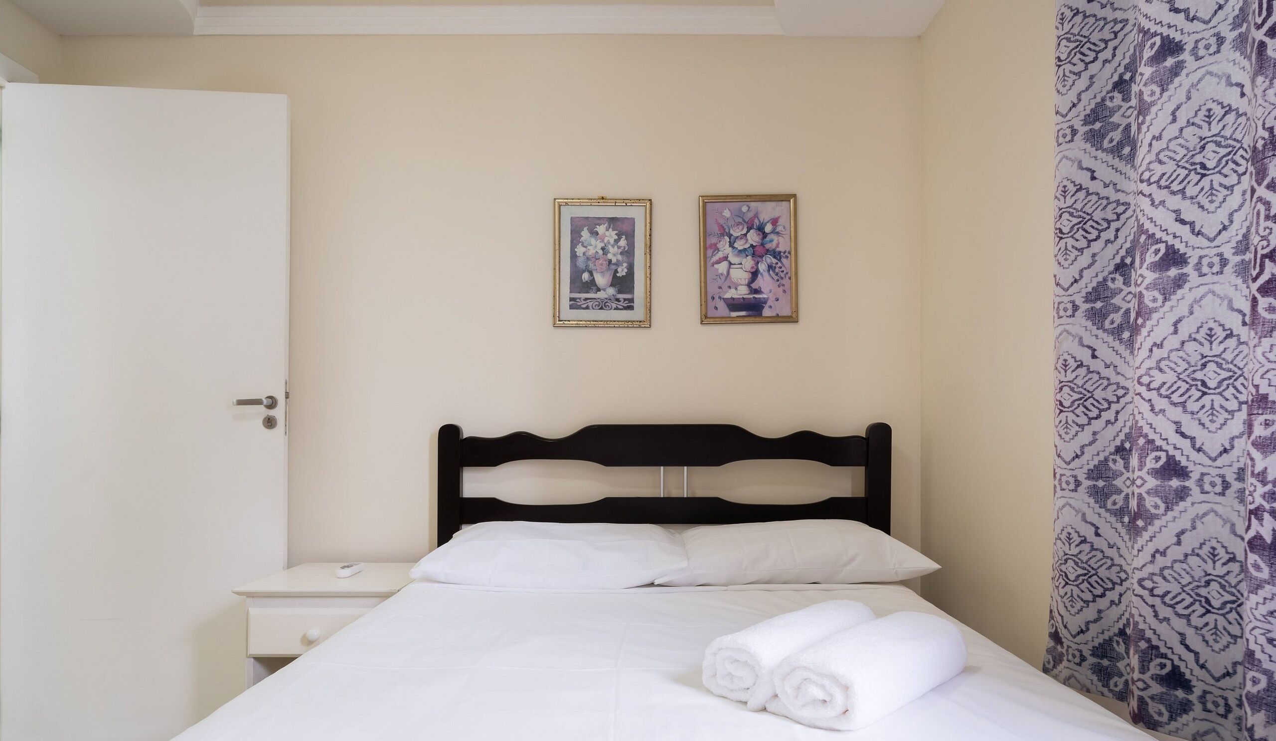 A hotel room with a bed, a nightstand, and two framed pictures on the wall.