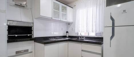 A kitchen with white cabinets, a black countertop, a stainless steel range hood, and a refrigerator.