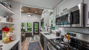 A modern kitchen with stainless steel appliances, a black stove, and a wooden ceiling. - Tiny Bear Paw-relax, unwind and recharge (Mentone)