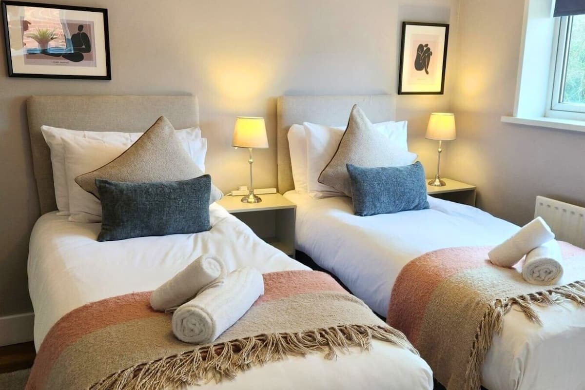 A hotel room with two beds, each with a headboard, bedside tables, lamps, and towels.