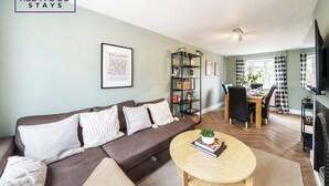 A living room with a sofa, a round coffee table, a bookshelf, and a dining area with a table and chairs. - Link Road House By REDWOOD STAYS (Alton)