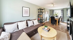 A living room with a sofa, a round coffee table, a bookshelf, and a dining area with a table and chairs. - Link Road House By REDWOOD STAYS (Alton)