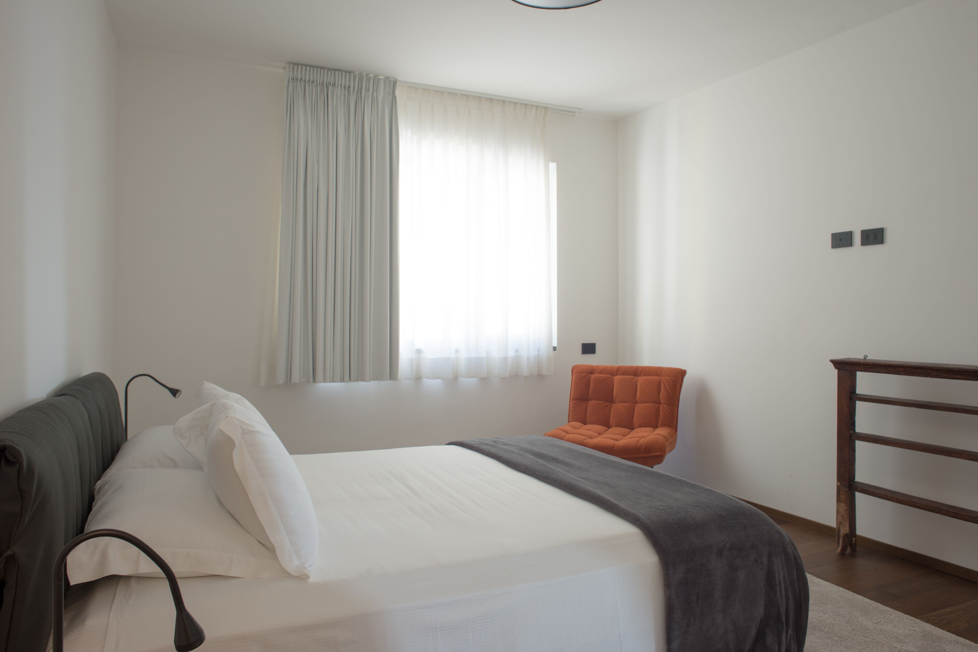 Un dormitorio con una cama, una silla, un escritorio y una ventana con cortinas.