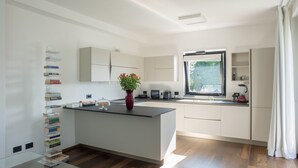 A modern kitchen with a central island, a built-in microwave, and a window with a view of greenery. - Villa Olivo (Blevio)