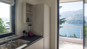 A modern kitchen with a built-in sink, a red blender, and a view of a lake and mountains through a large window. - Villa Olivo (Blevio)