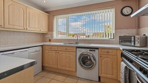 Een keuken met houten kastjes, een wasmachine, een fornuis en een raam met jaloezieën.