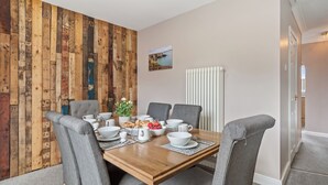 Een eethoek met een houten wand, grijze gestoffeerde stoelen, een houten tafel en een witte radiator.