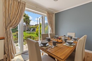 A dining area with a wooden table set for breakfast, including bowls, mugs, and croissants. - Sea Charm - Cosy Bungalow, Near Beach and Village (Saundersfoot)