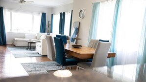 A modern living room with a dining area, featuring a wooden dining table, blue chairs, a white sofa, and a large window with curtains. - Modern 2BR Condo in Gatlinburg (Gatlinburg)