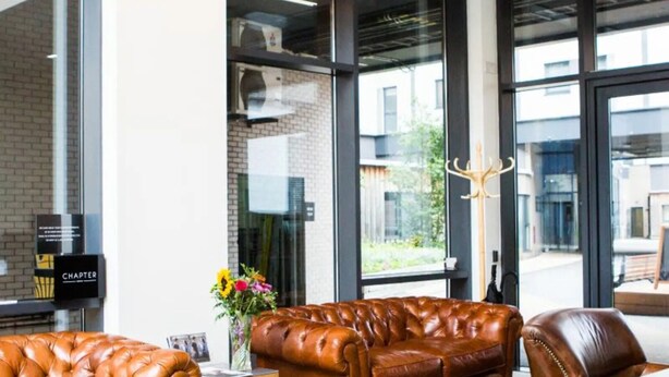A modern interior with leather sofas, a wooden table, and large windows offering views of the outside. - For Students Only Chapter Highbury I in London (London)
