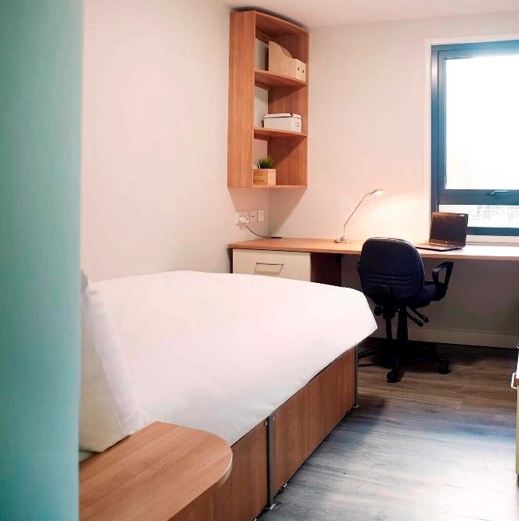 A bedroom with a bed, a desk, a chair, and a window.