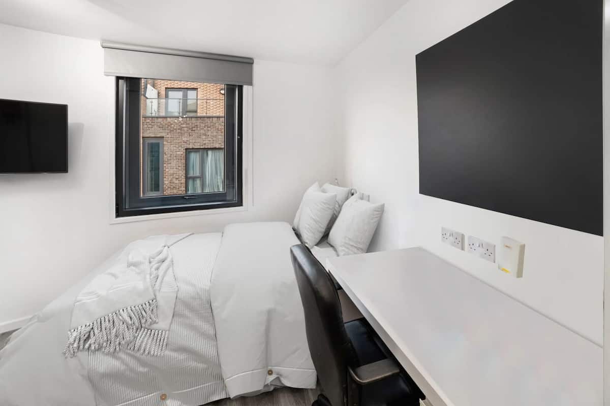 A modern, minimalist bedroom with a bed, a desk, and a TV.