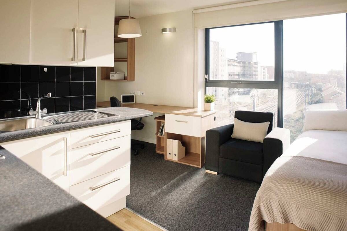 A modern, compact apartment with a kitchenette, a dining area, a workspace, and a seating area with a view of the city.