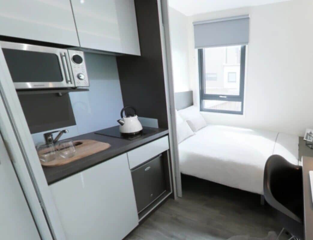 Quarto compacto com cozinha compacta, uma cama e uma janela.