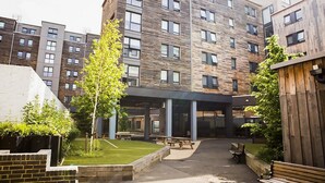 A modern apartment building with a courtyard featuring a lawn, benches, and a wooden fence. - For Students Only Chapter Highbury I in London (London)