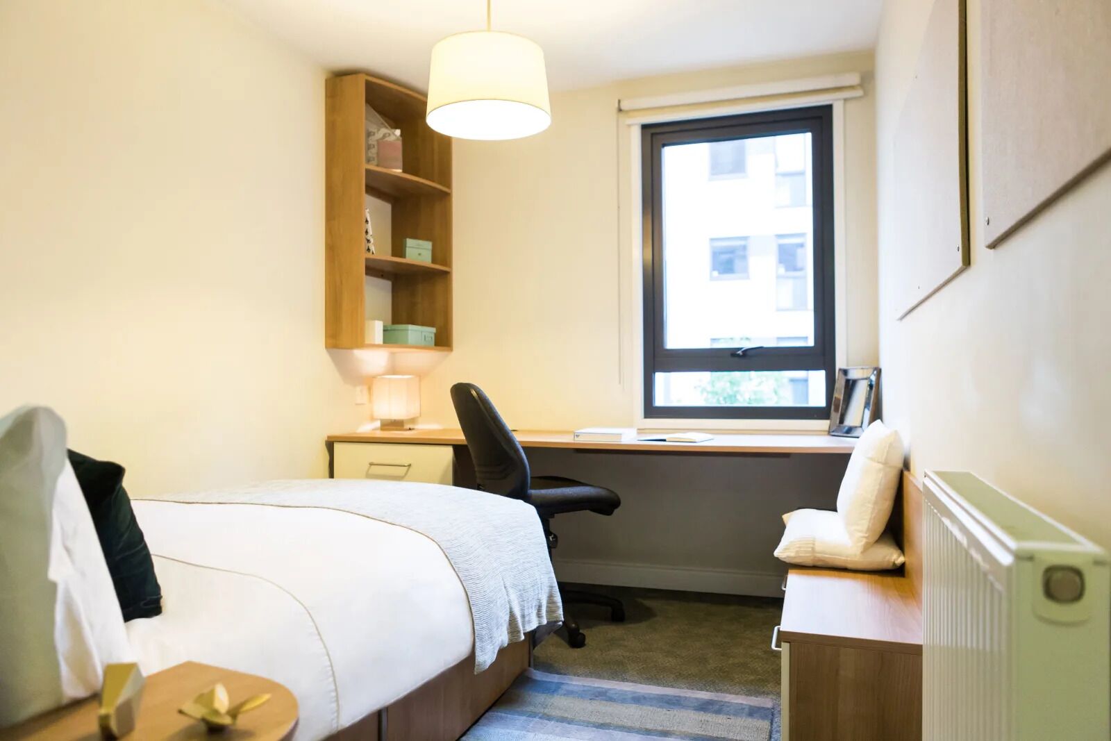 A bedroom with a bed, a desk, a chair, a lamp, a shelf, and a window.