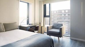A modern hotel room with a large bed, a desk with a chair, a small armchair, and a large window offering a city view. - For Students Only Chapter Highbury I in London (London)