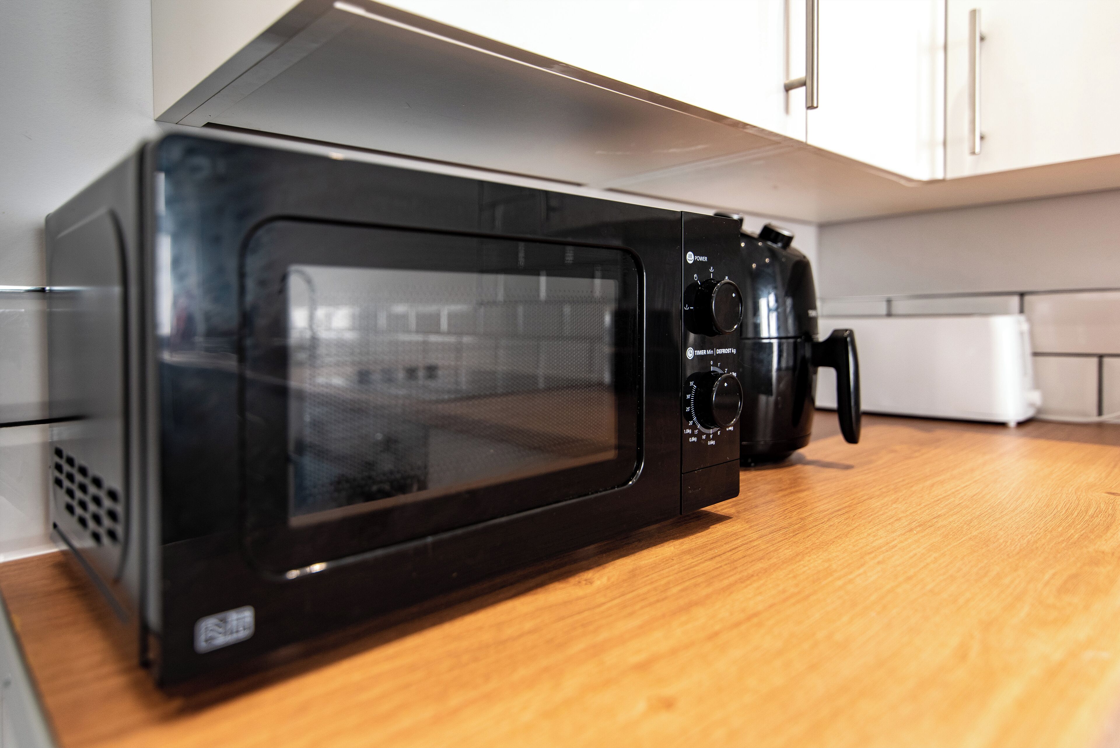 A black microwave oven on a wooden countertop in a kitchen with white cabinets.