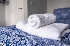 A neatly folded white towel on a bed with a blue patterned bedspread. - Maritime House II (Hull)