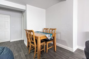 A dining area with a wooden table and chairs, a white door, and a gray floor. - Maritime House II (Hull)