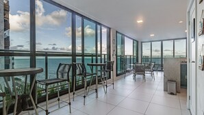 Ein geräumiger Balkon mit großen Fenstern und Meerblick. Mehrere Stühle und ein kleiner Tisch sind vorhanden.