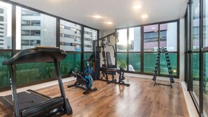 Ein Fitnessstudio mit Trainingsgeräten, großen Fenstern und Blick auf Gebäude.