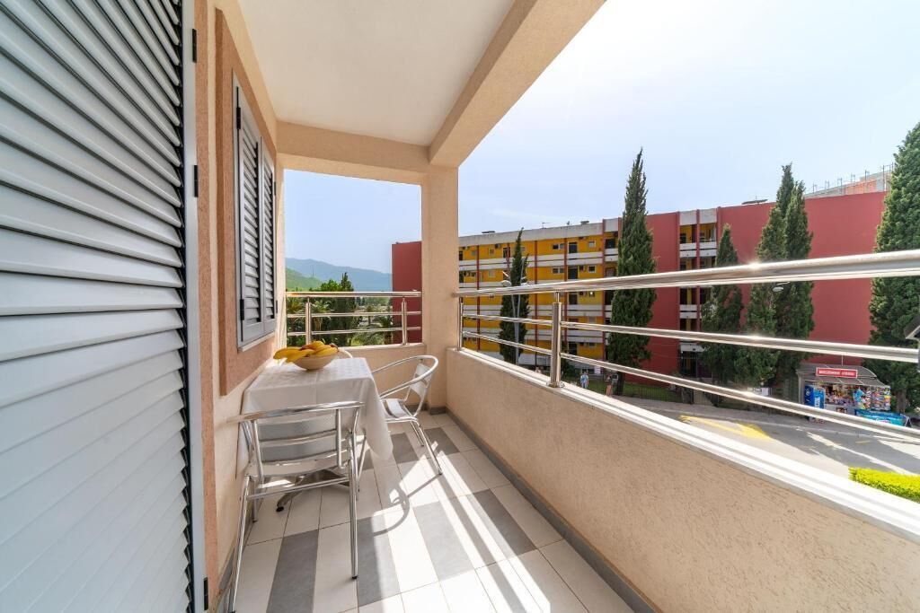 A balcony with a table and chairs, a view of a red building, and a clear sky.