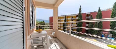 A balcony with a table and chairs, a view of a red building, and a clear sky.