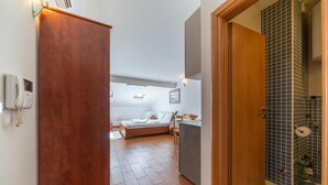 Hotellihuone, jossa on puinen ovi, sänky, pieni pöytä ja sinisillä laatoilla päällystetty kylpyhuone.